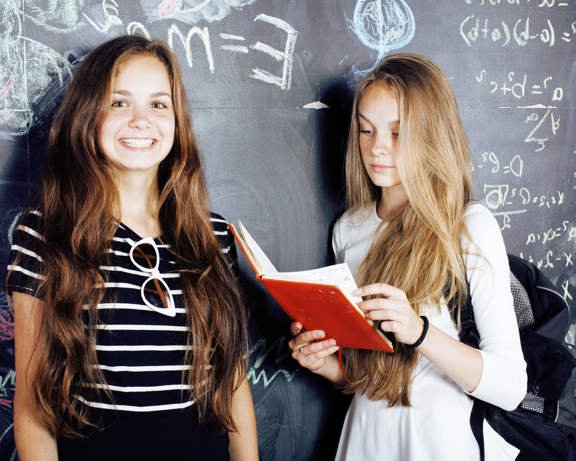 back to school after summer vacations, two teen real girls in classroom with blackboard painted together close up